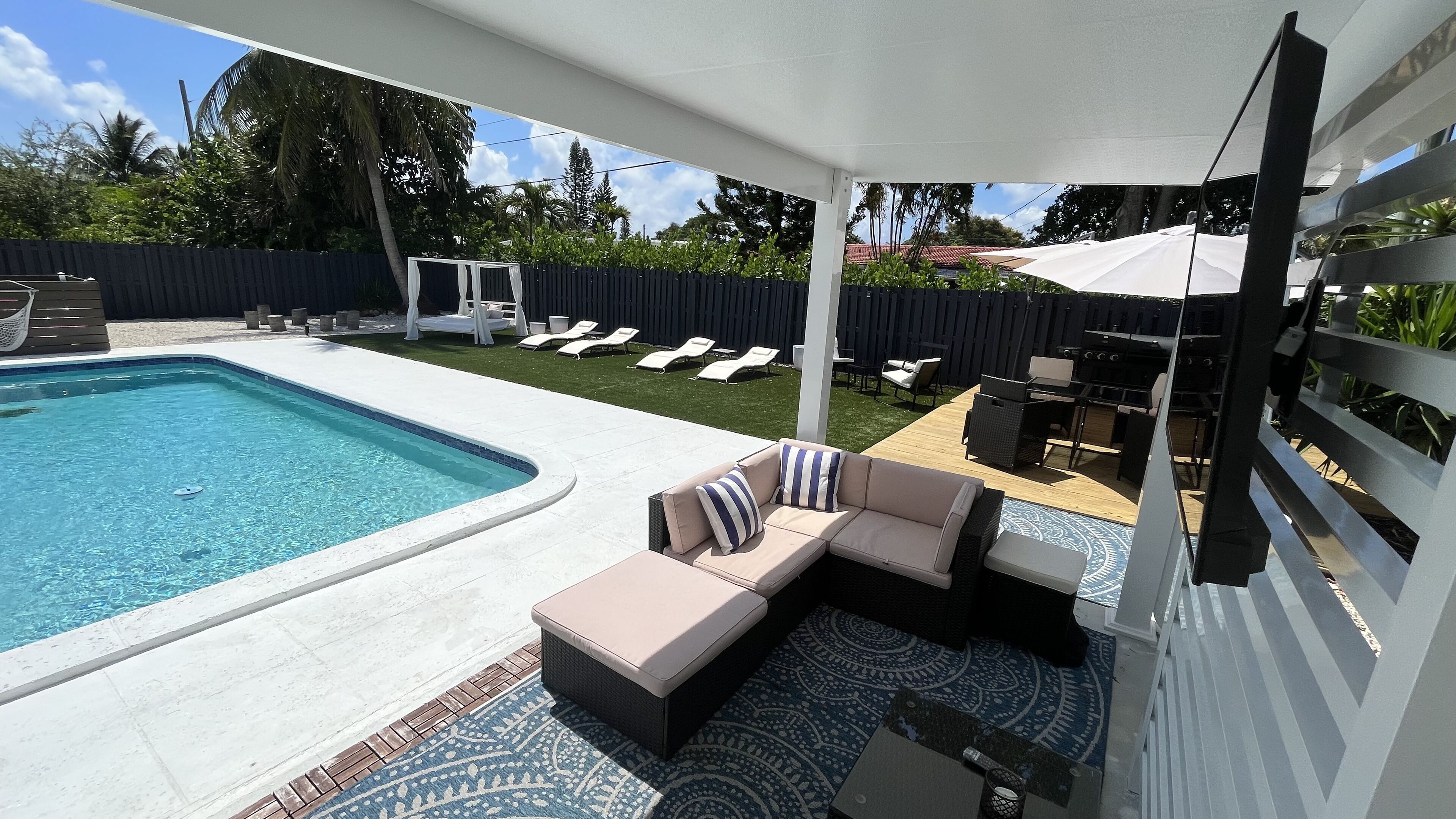 A backyard with a swimming pool, a covered seating area, and a barbecue grill.