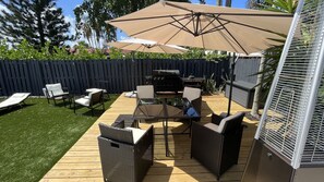 Relax in the shaded patio area with lounge chairs and wicker furniture, surrounded by a wooden fence.