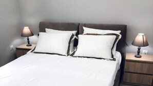 A neatly made bed with white linens and two bedside lamps on wooden nightstands. - Charming Apartment in Faliro (Palaio Faliro)