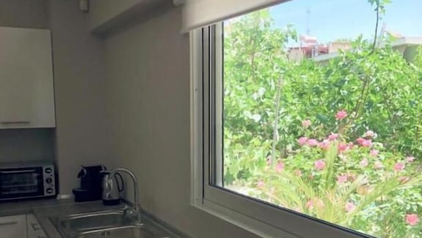 A kitchen with a large window, a sink, and a countertop with a fruit bowl. - Charming Apartment in Faliro (Palaio Faliro)