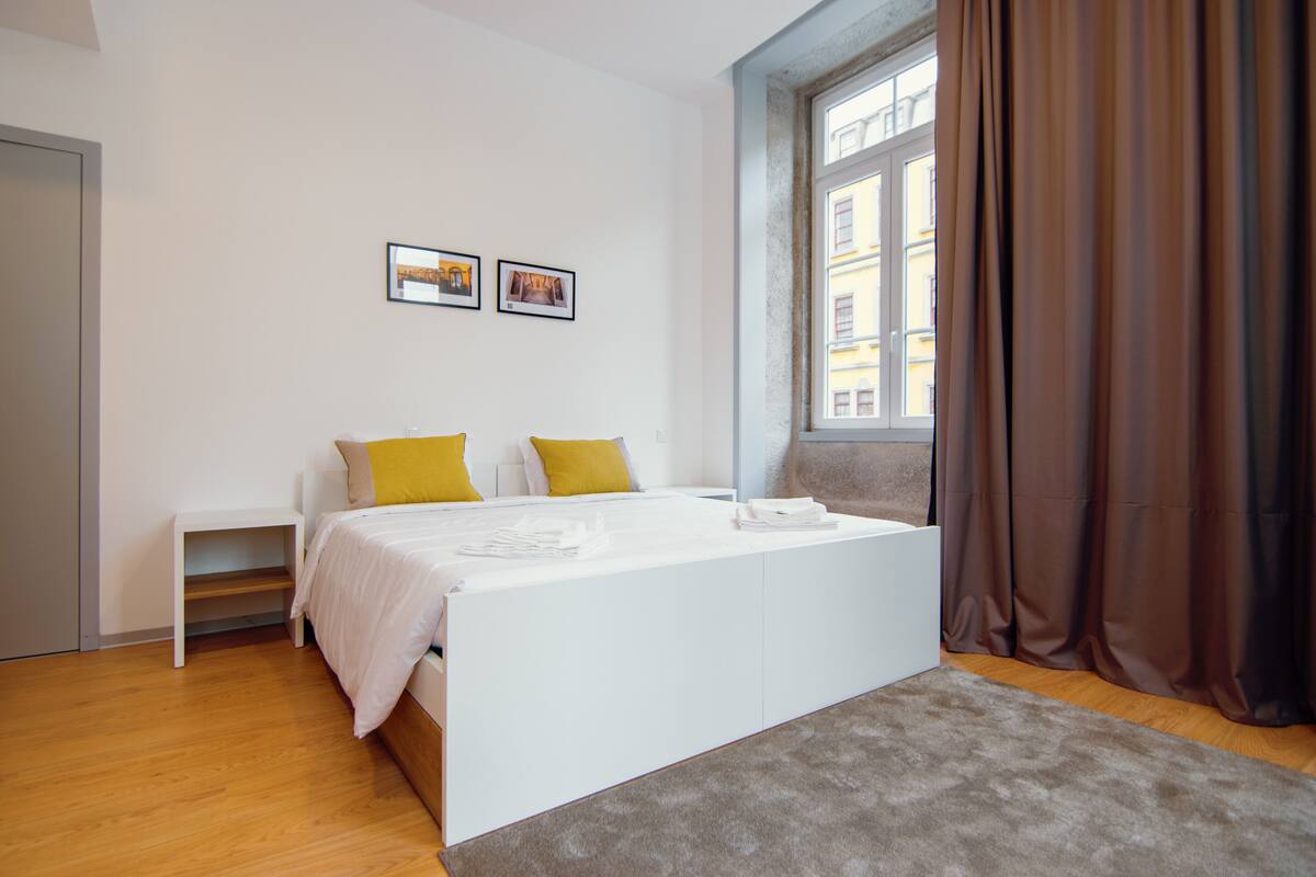 Une chambre à coucher moderne avec un lit, des tables de chevet et une fenêtre avec des rideaux.