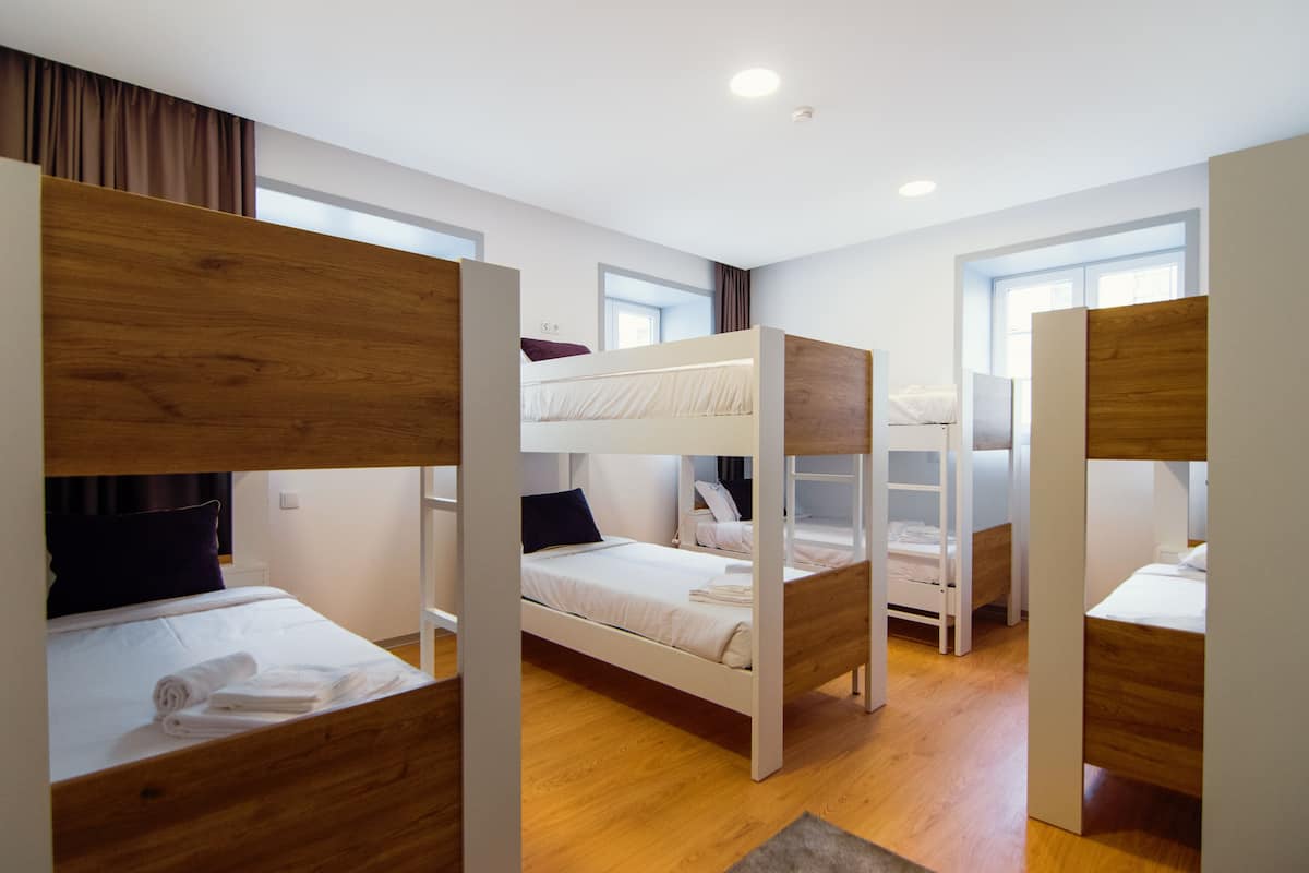Une chambre de dortoir avec des lits superposés, des cloisons en bois et une fenêtre laissant entrer la lumière naturelle.