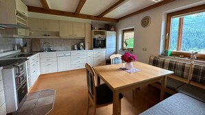 A compact kitchen with modern appliances, a dining area with a bench, and a window with a view of greenery. - Vacation apartment on the farm (Wald)