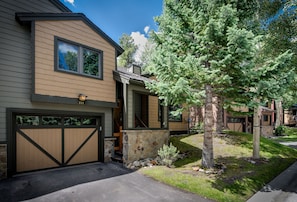 A two-story house with a stone entryway, a garage with a wooden door, and a large tree in the front yard.