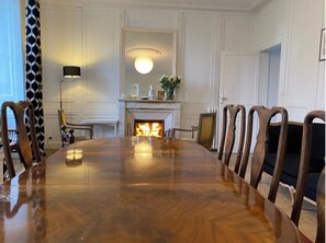 Formal dining room with a large conference table and six chairs, a fireplace, and a high ceiling with decorative molding.