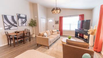 A modern living room with a sofa, coffee table, TV, and dining area with chairs and a table.
