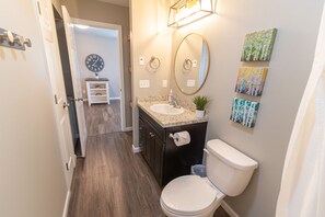 A bathroom with a white toilet, a sink with a granite countertop, a mirror, and a clock on the wall.