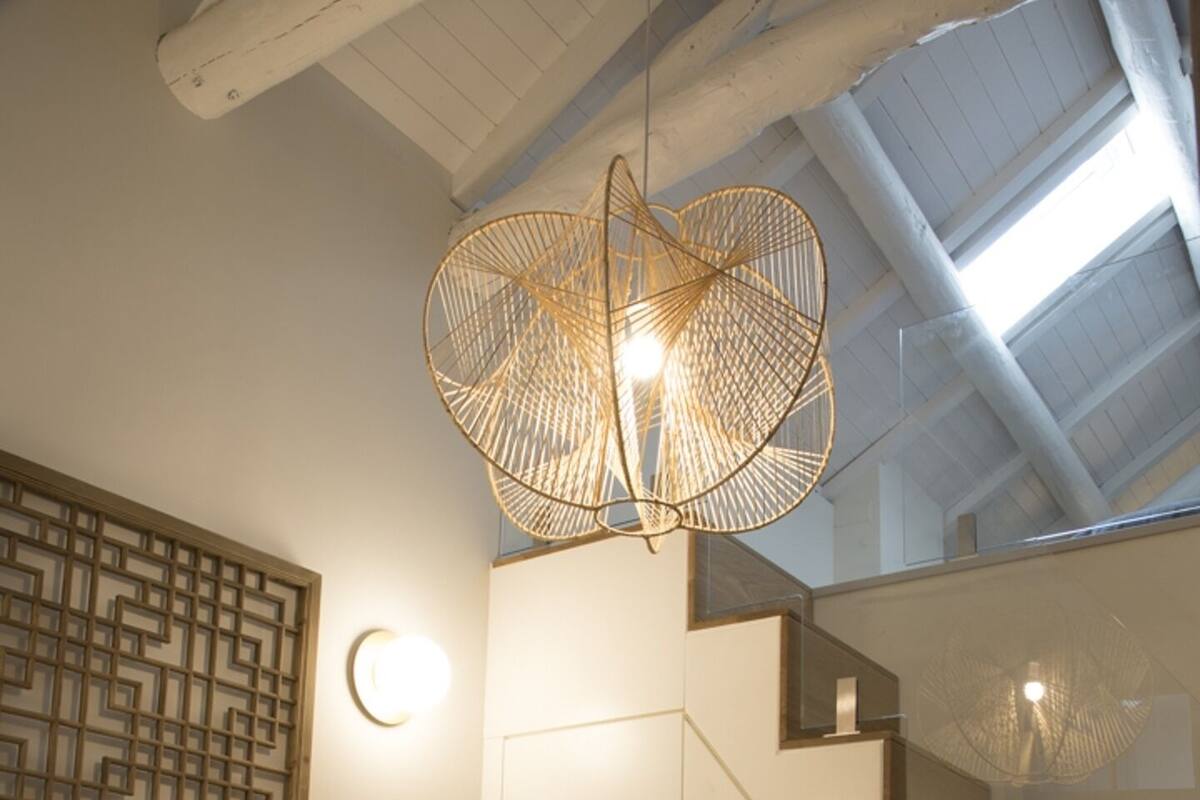 A modern bedroom with a bed, a geometric wall decoration, a staircase, and a unique woven light fixture.