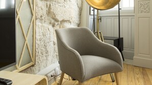 A room with a stone wall, a modern chair, a floor lamp, and a TV on a wooden stand. - Top Porto (Porto)