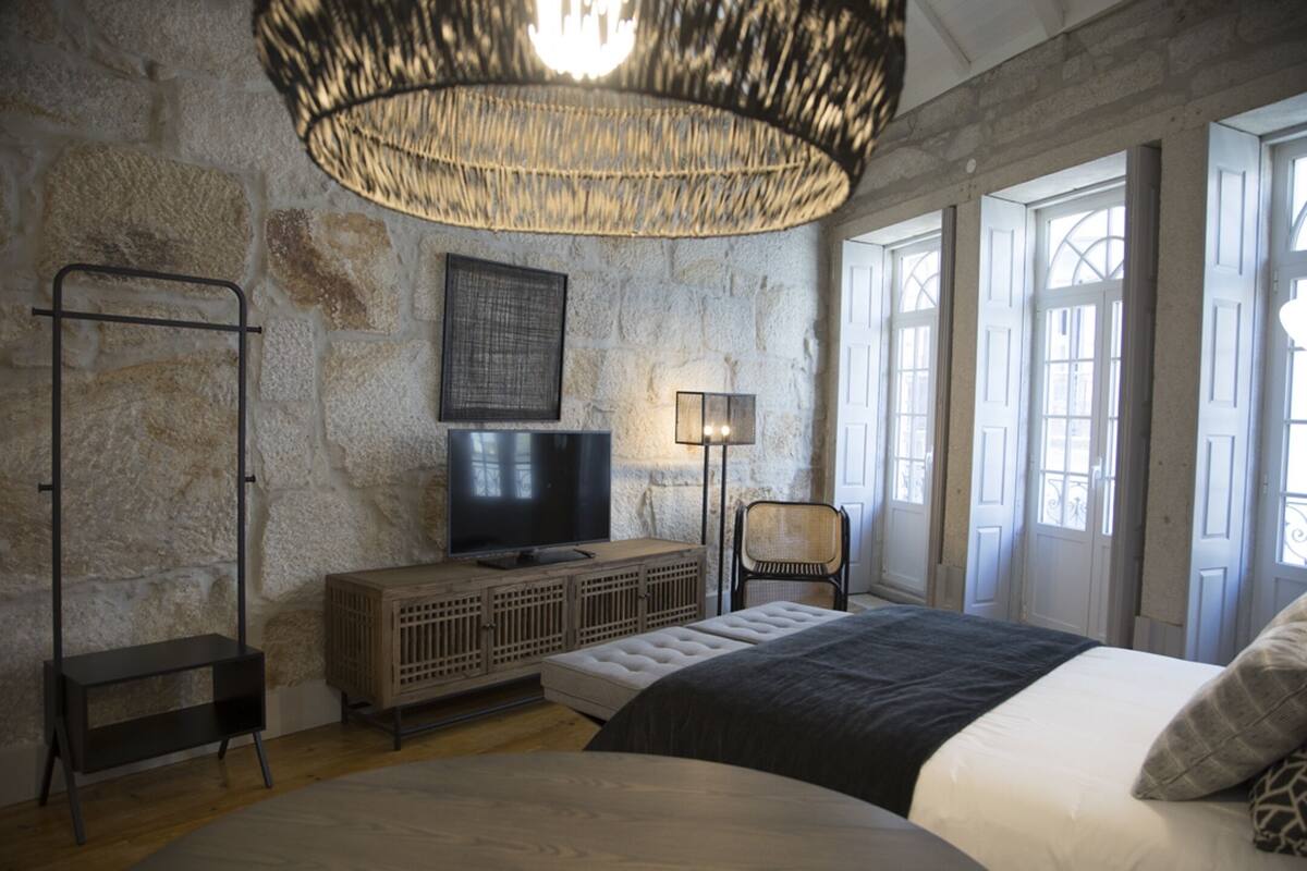 A bedroom with a large bed, a television, a lamp, and a stone wall.