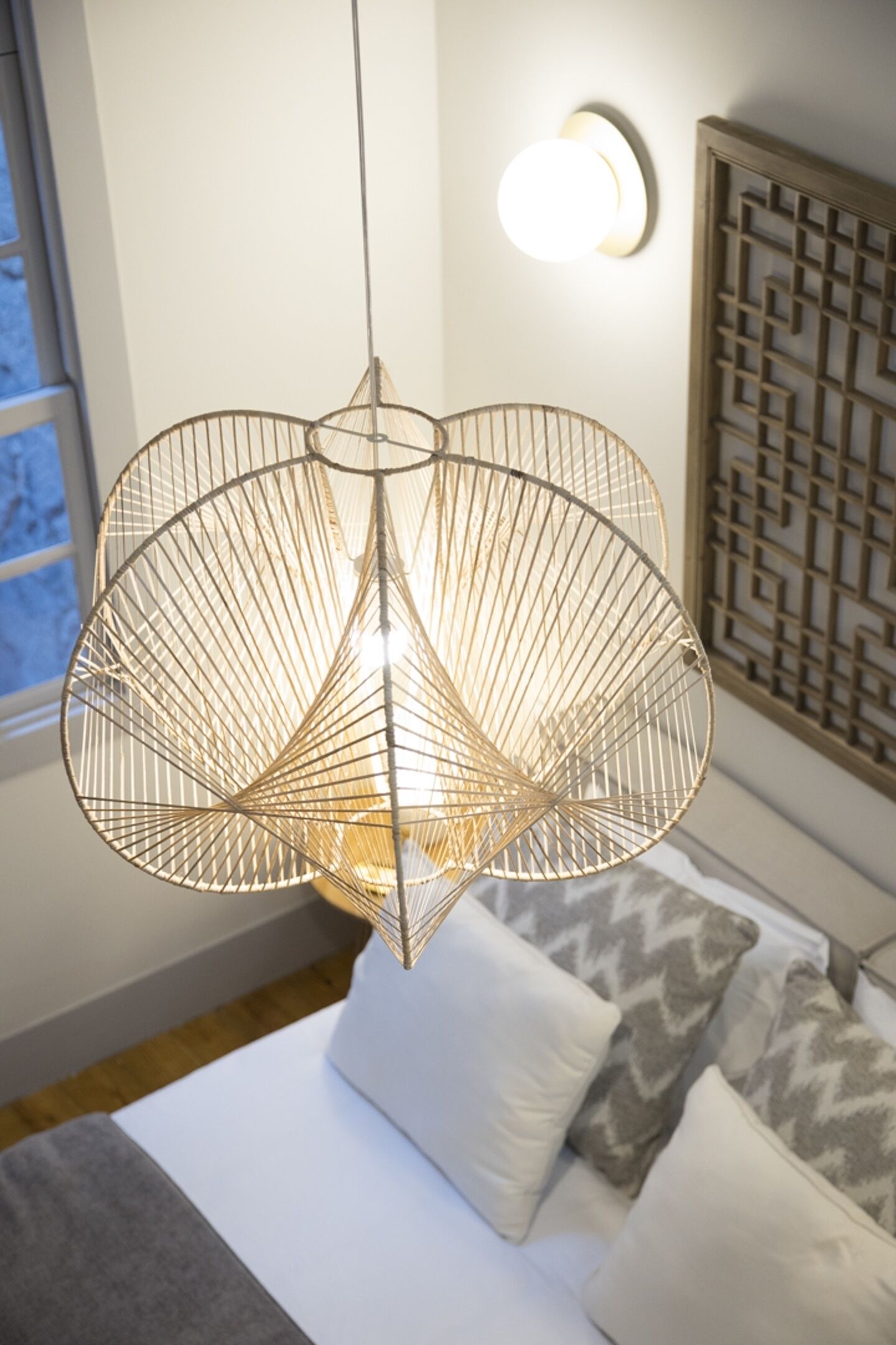 Una camera da letto moderna con una lampada a sospensione, un letto con cuscini decorati e un pannello parete decorativo.