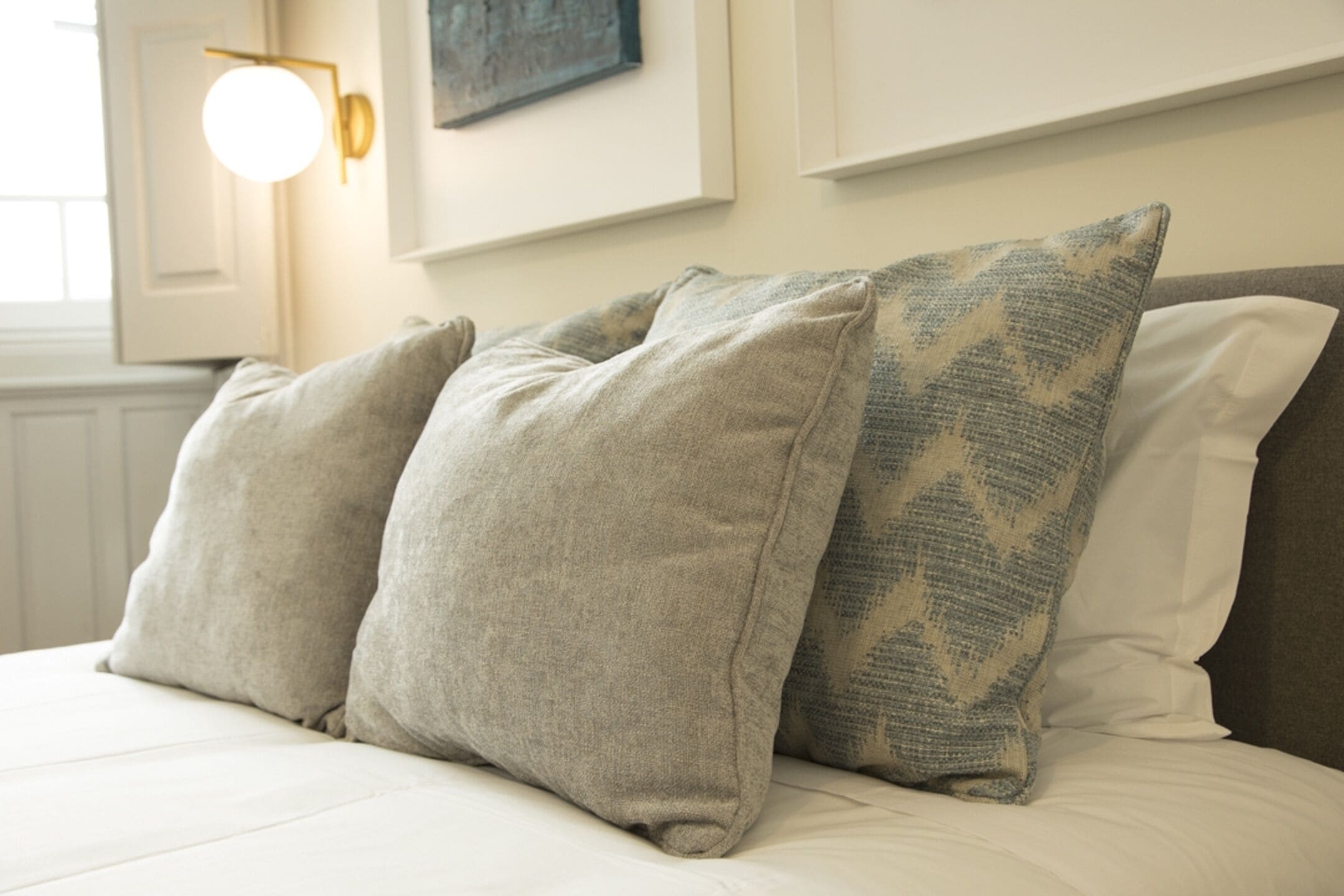 Una cama con tres almohadas y una lámpara de pared.