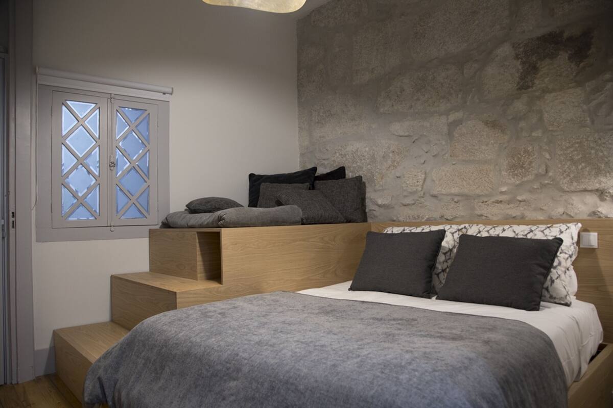 A bedroom with a bed, a window with a view, and a stone wall.