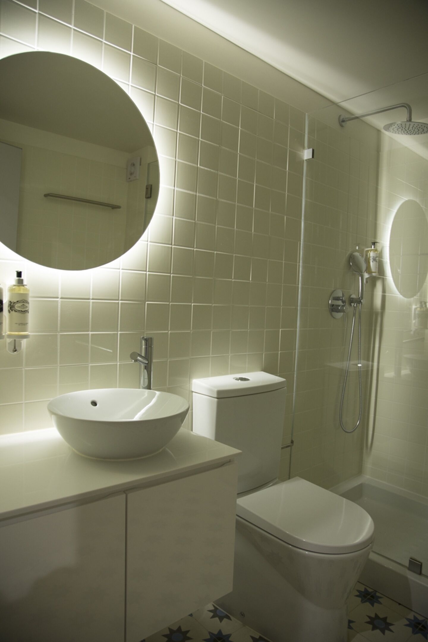 Une salle de bain avec un miroir rond, un lavabo sur colonne, des toilettes et un espace douche.