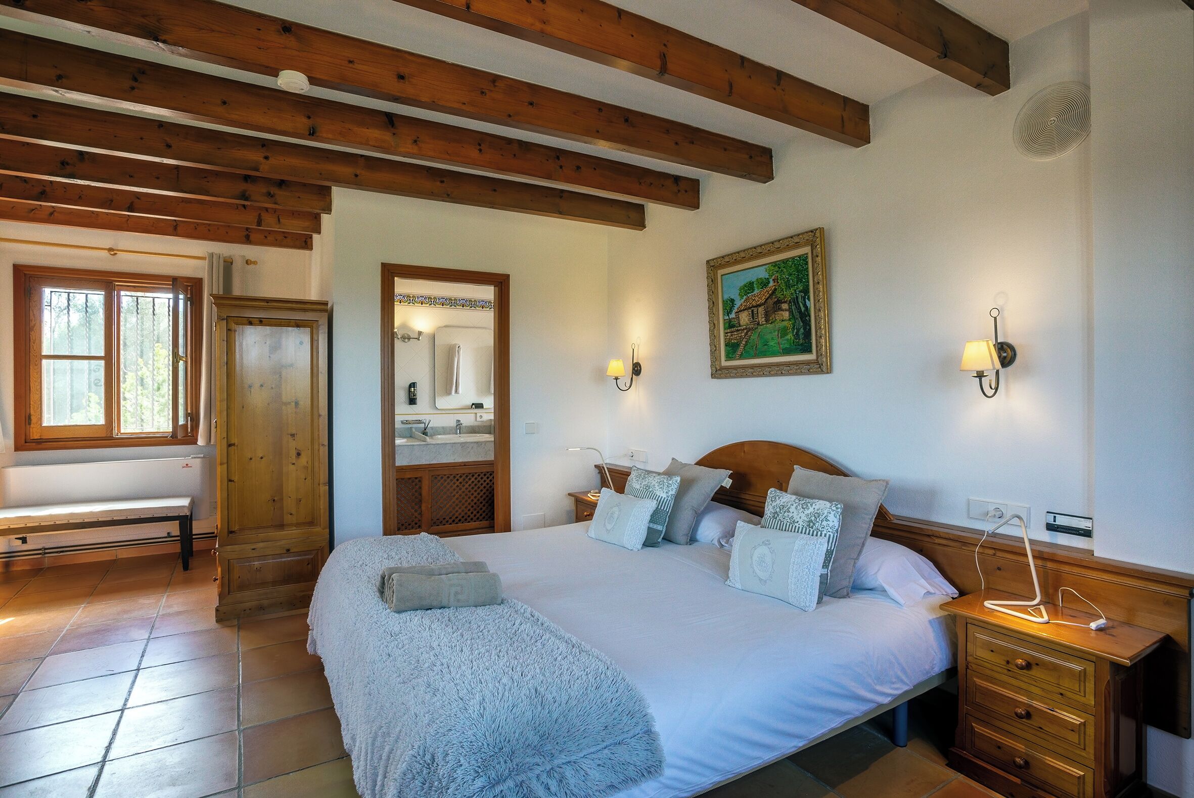 Un dormitorio con una cama grande, vigas de madera, un banco, un espejo y un cuadro.