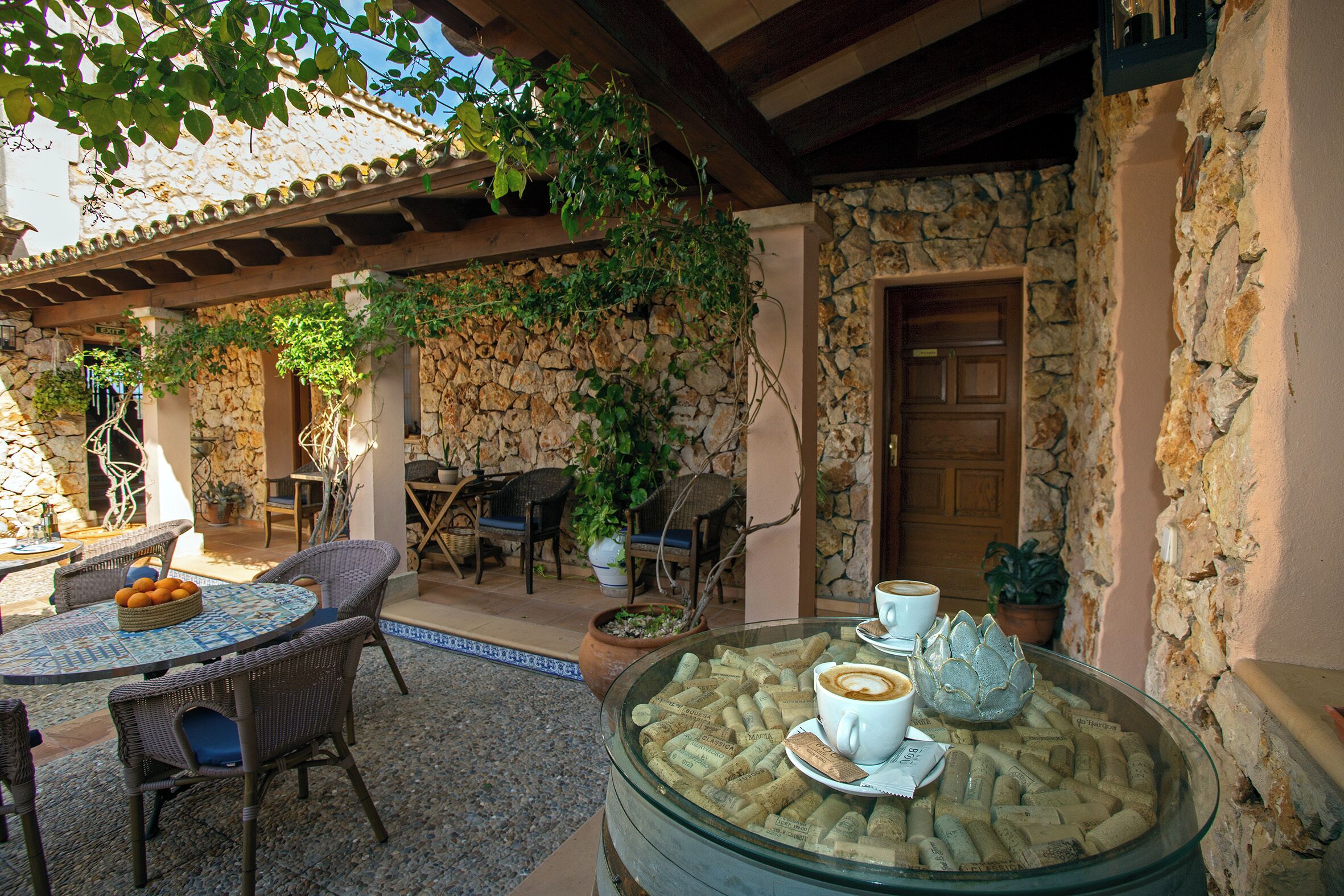 A patio area with wicker furniture, a glass table with wine corks, and a stone wall.