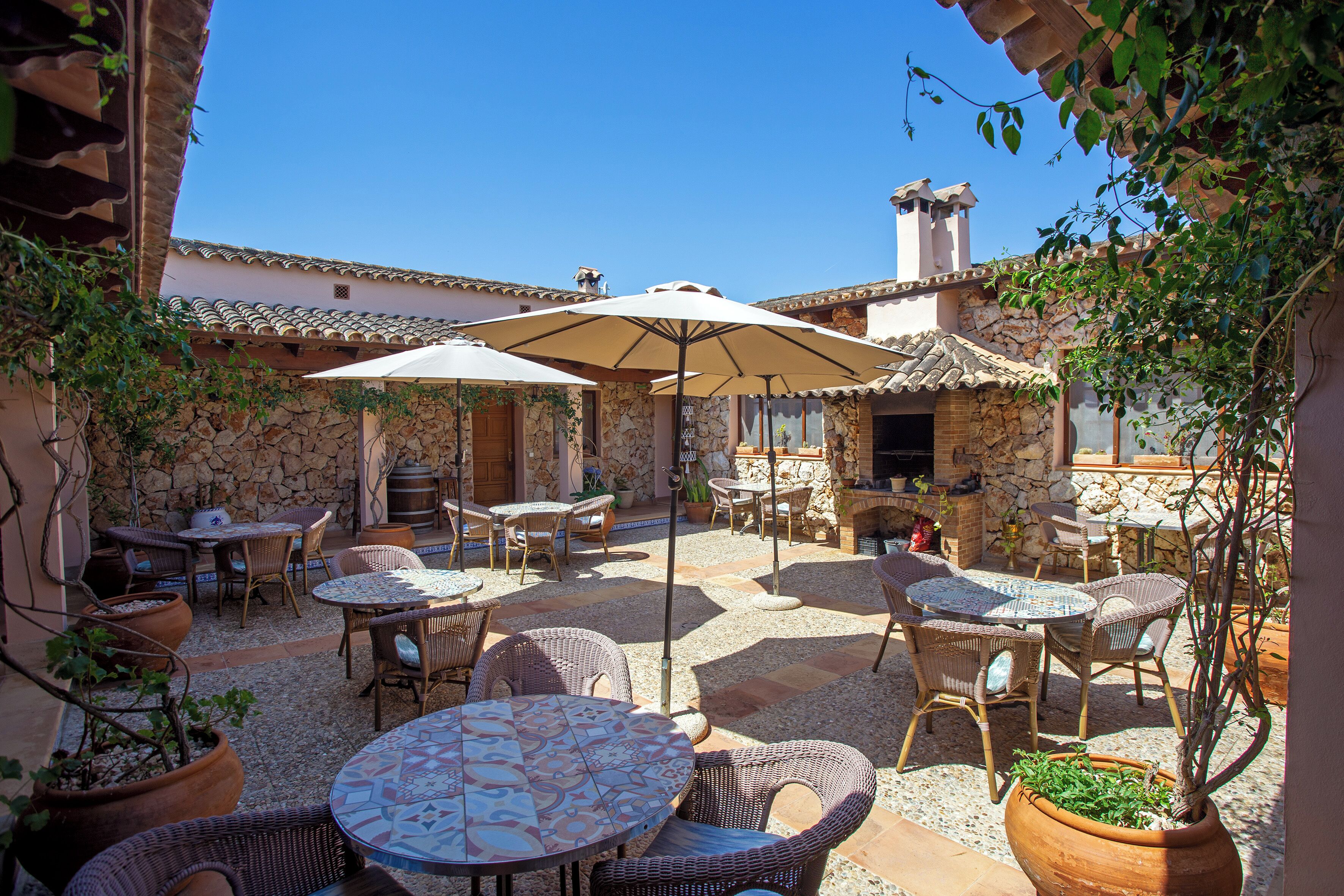 An outdoor patio with wicker furniture, stone walls, and a clear blue sky.
