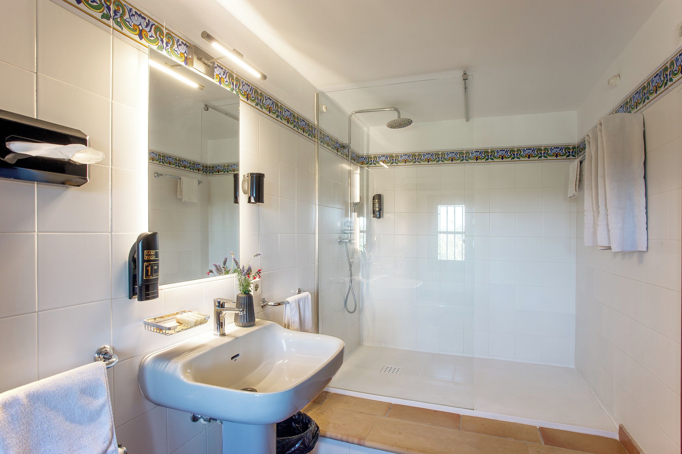 Un baño con lavabo, espejo, toallero y ducha.