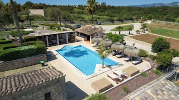 Une piscine avec des chaises longues, un bâtiment en pierre et une vue sur le paysage environnant.