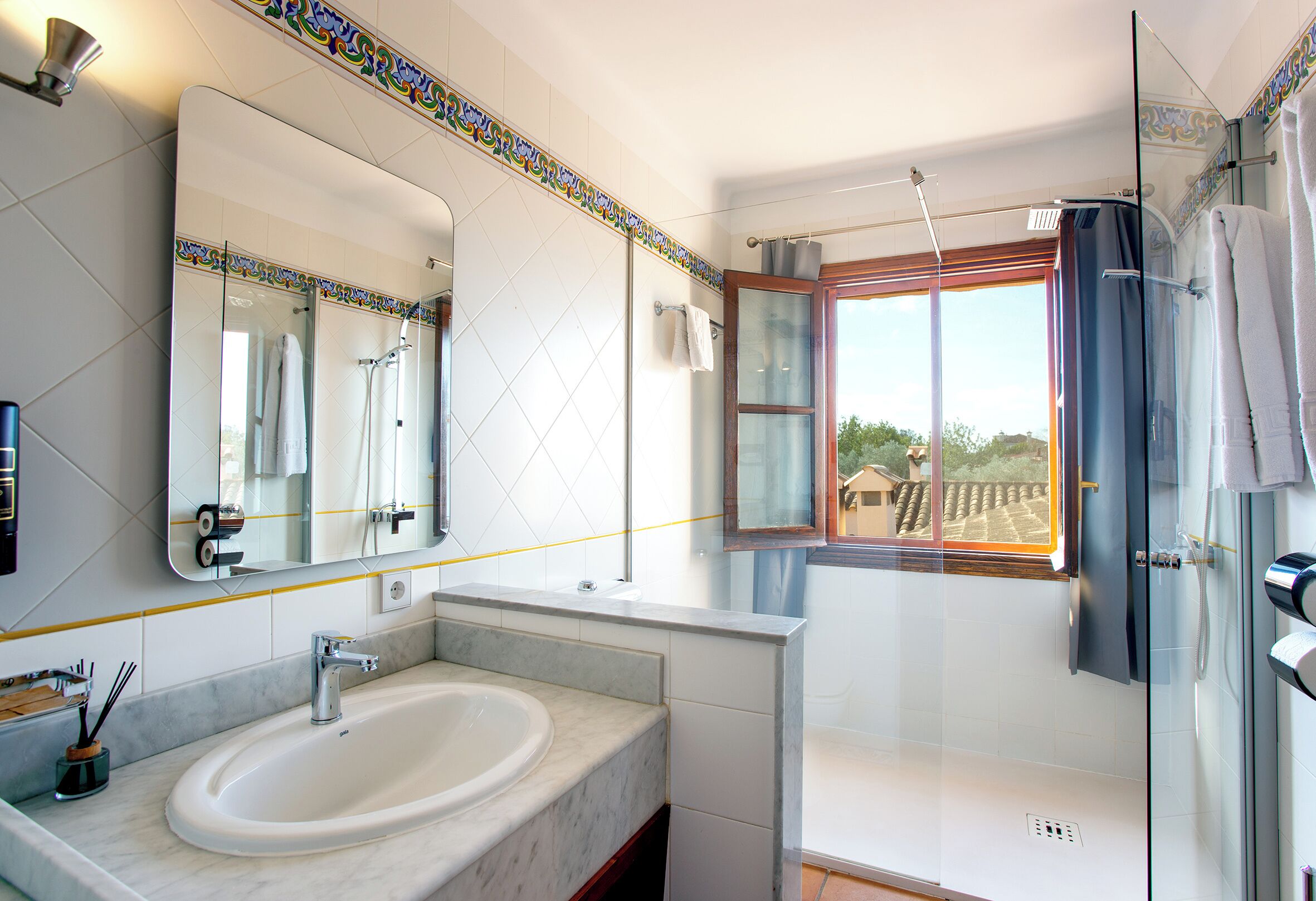 A bathroom with a large mirror, a sink, a shower, and a window.