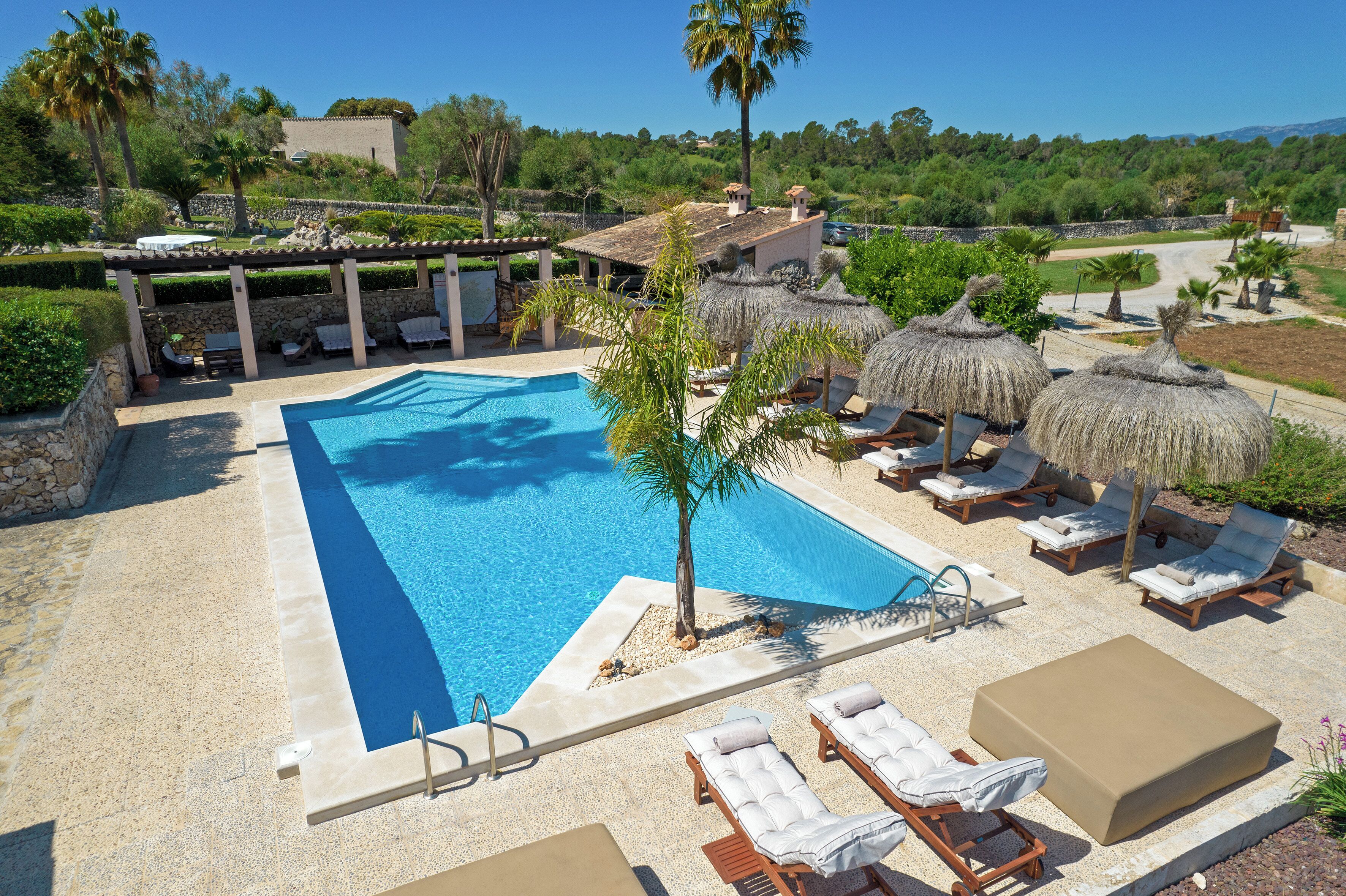 A swimming pool with lounge chairs and umbrellas, surrounded by greenery and a stone building.