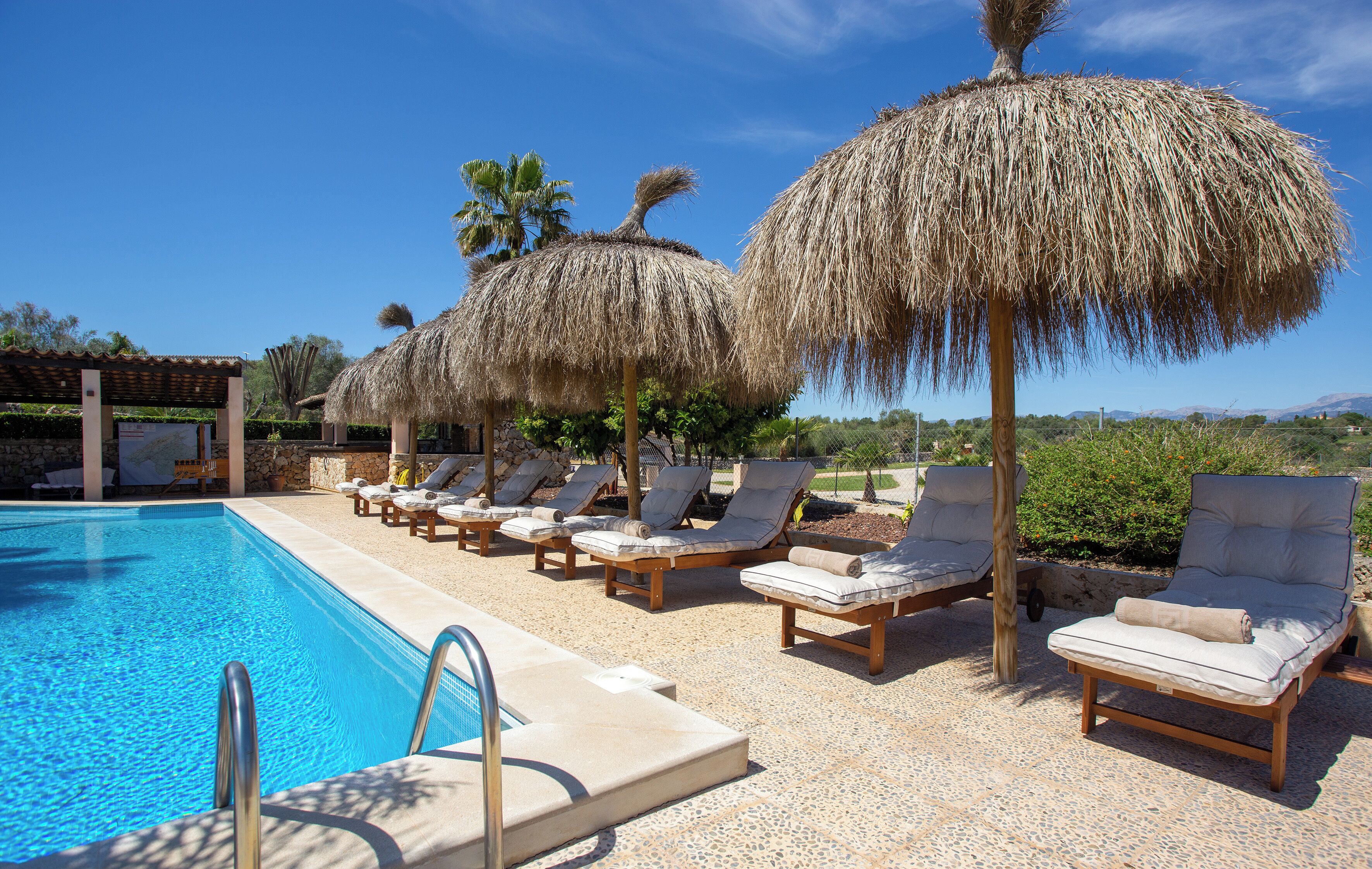 Uma área de piscina com espreguiçadeiras e guarda-sóis de palha.