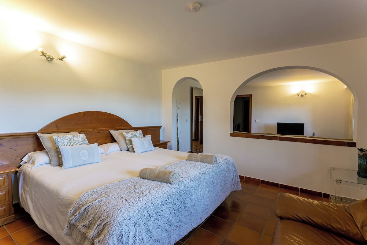 Une chambre à coucher avec un grand lit, une tête de lit en bois, une table de chevet, une table en verre et un miroir au mur.
