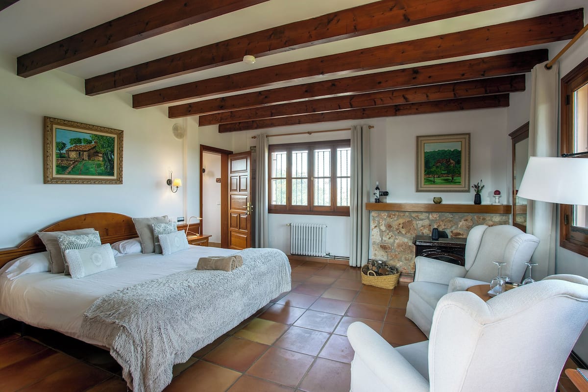 Une chambre à coucher avec un lit, une chaise, une cheminée et des poutres en bois au plafond.