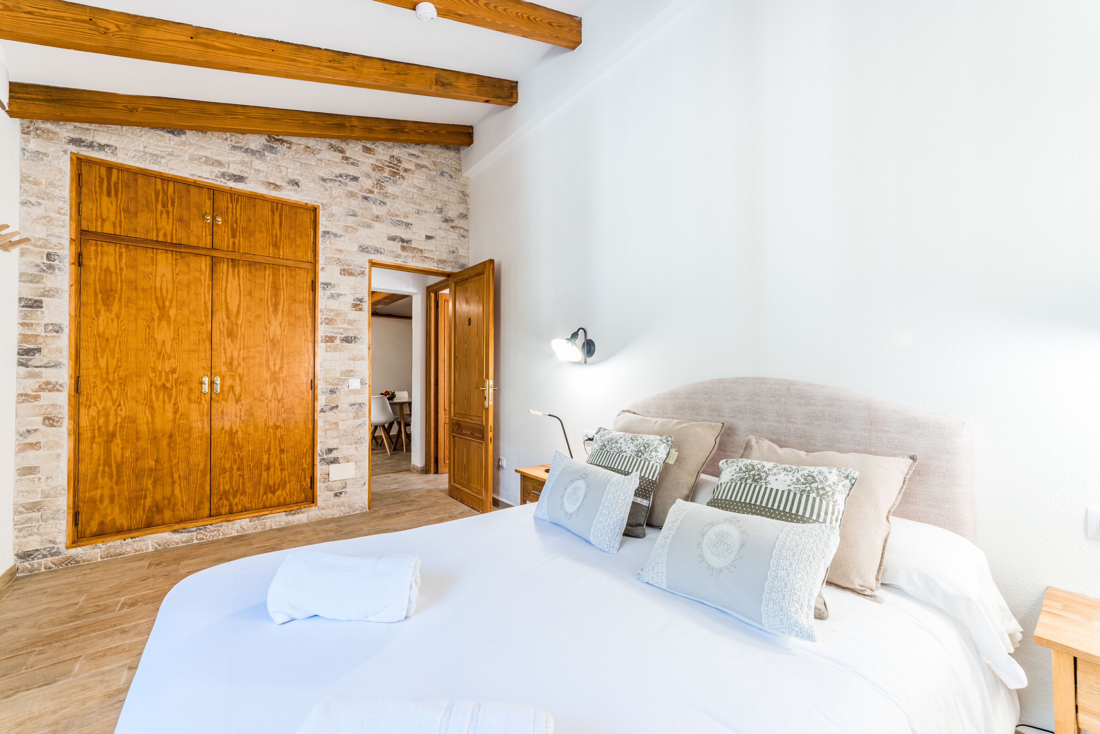 A bedroom with a large bed, wooden wardrobe, stone wall, and a wooden ceiling beam.