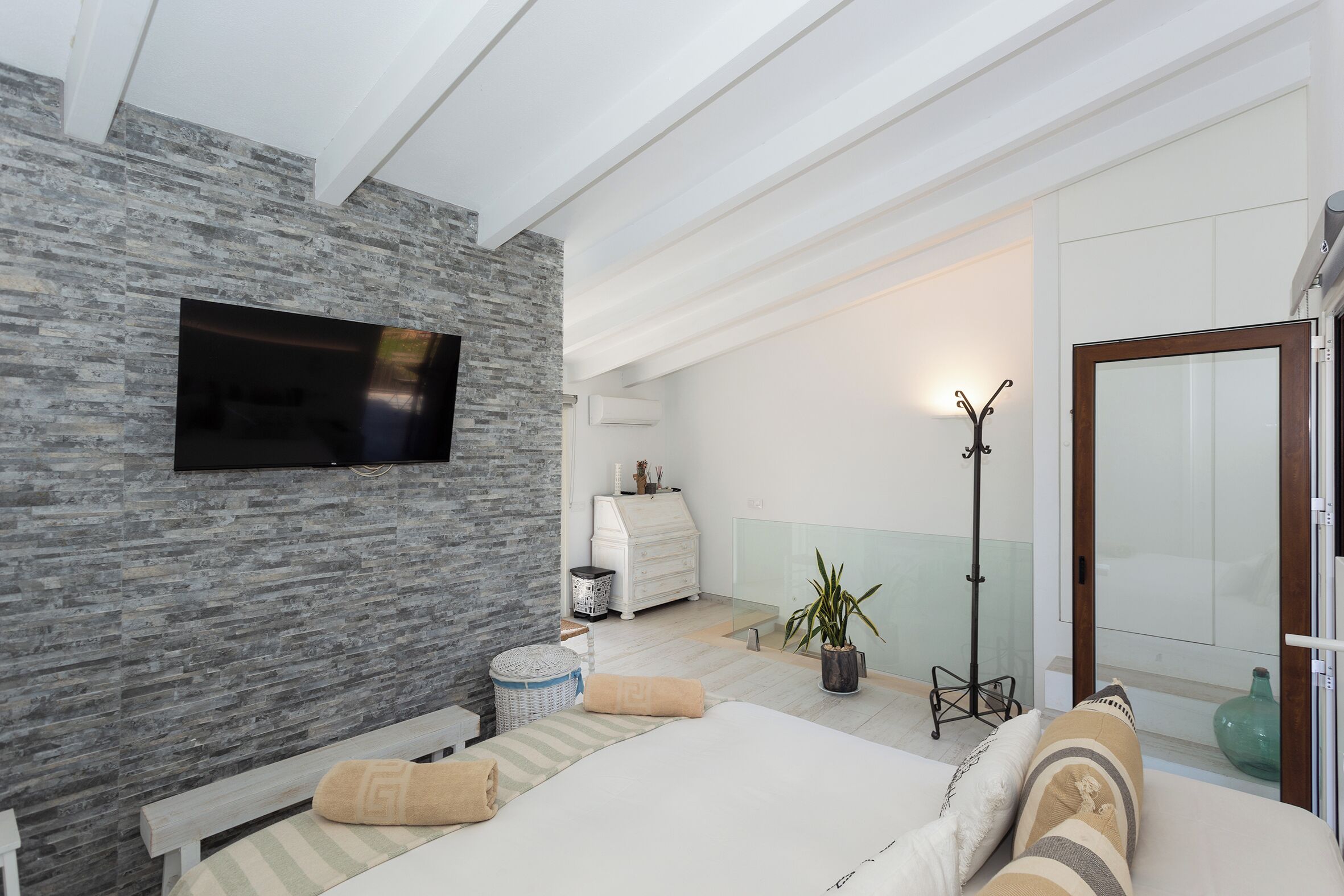 Un dormitorio con pared de piedra, una cama, un televisor, una mesita de noche, una lámpara, una planta en maceta y un armario.