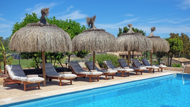 Une piscine avec des chaises longues et des parasols en chaume.