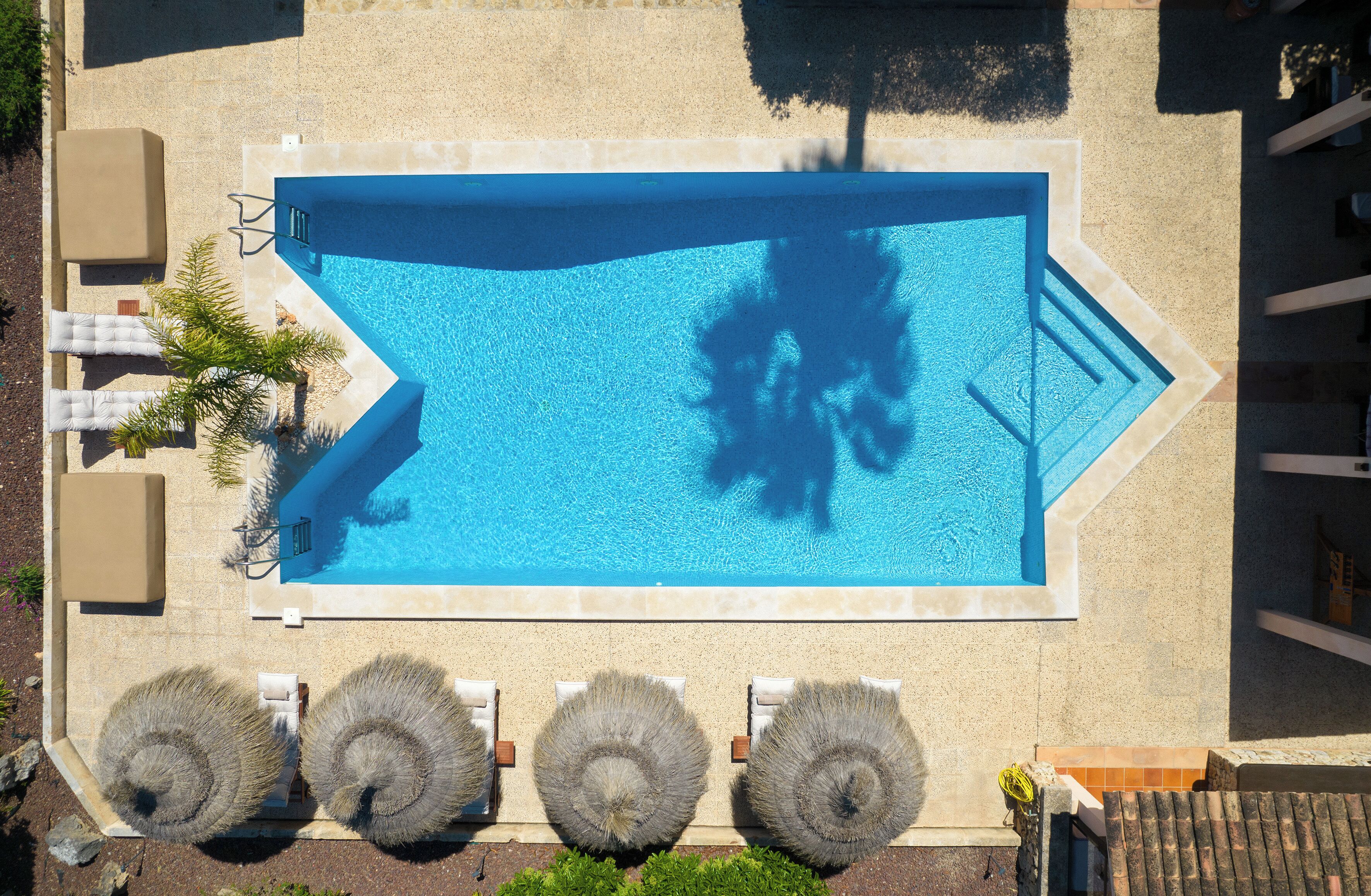 Vista aérea de una piscina rectangular con solárium empedrado, rodeada de sillones y tumbonas.