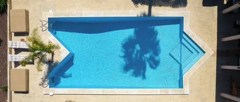 An aerial view of a rectangular swimming pool with a tiled deck, surrounded by lounge chairs and sun loungers.