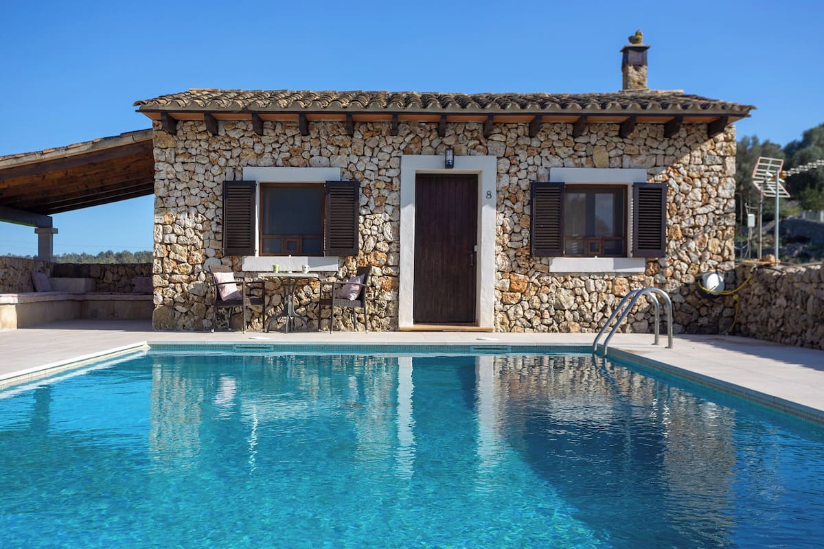 Un bâtiment en pierre doté d’une piscine, d’une porte et de deux fenêtres avec volets.