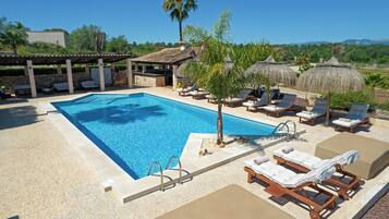 Un área de piscina con sillas de descanso, una palmera y una estructura de techo de paja.