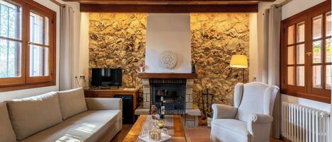 Una sala de estar con una pared de piedra, chimenea, sofá, sillón y televisor.