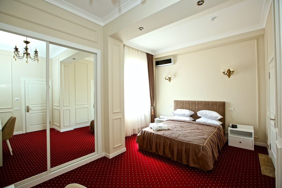 A hotel room with a large mirror, a bed with white linens, a red carpet, and a chandelier.