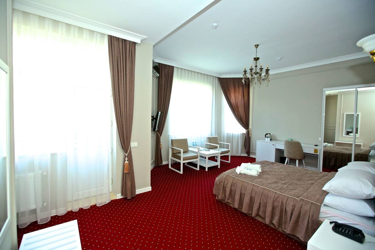 A hotel room with a bed, a desk, a chair, a small table, a mirror, and a red carpet.