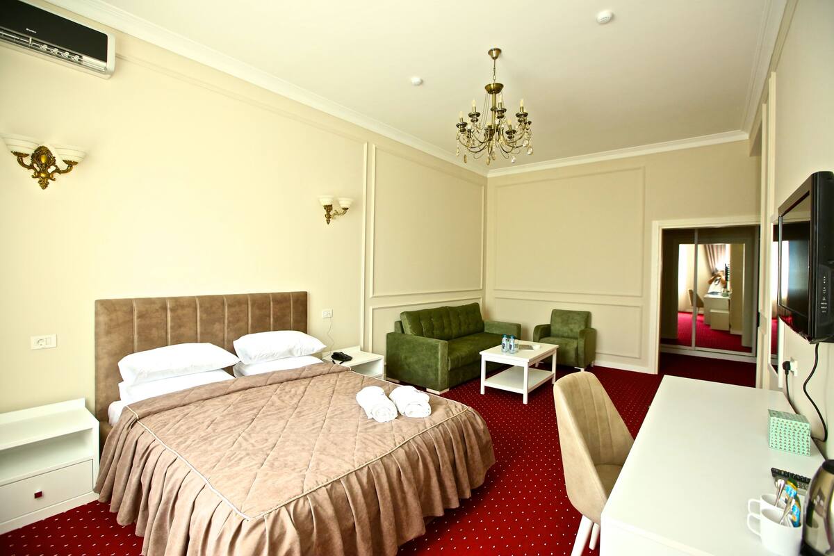 A hotel room with a large bed, a green sofa, a small table, and a TV.