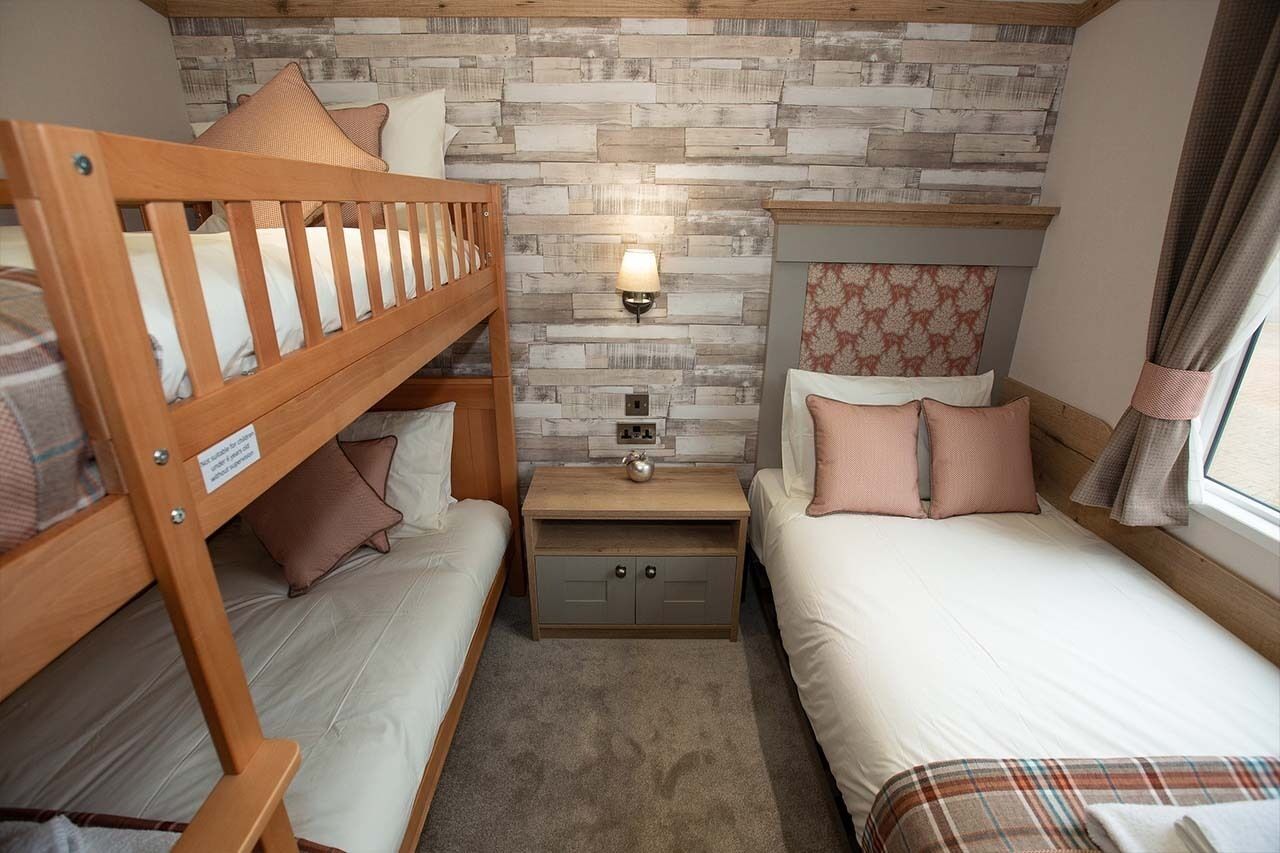 A bedroom with two beds, a nightstand, a wall-mounted lamp, and a patterned headboard.