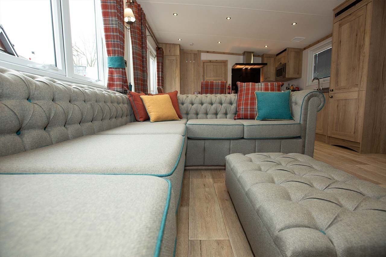 A cozy living area with a large sectional sofa, a smaller sofa, and a matching ottoman. There is a kitchen area with wooden cabinets and a microwave.