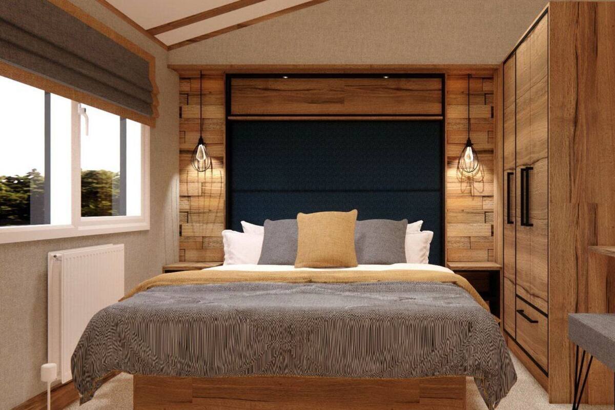 Quarto com cama grande, cabeceira de madeira, duas luminárias de cabeceira e vista para o exterior pela janela.