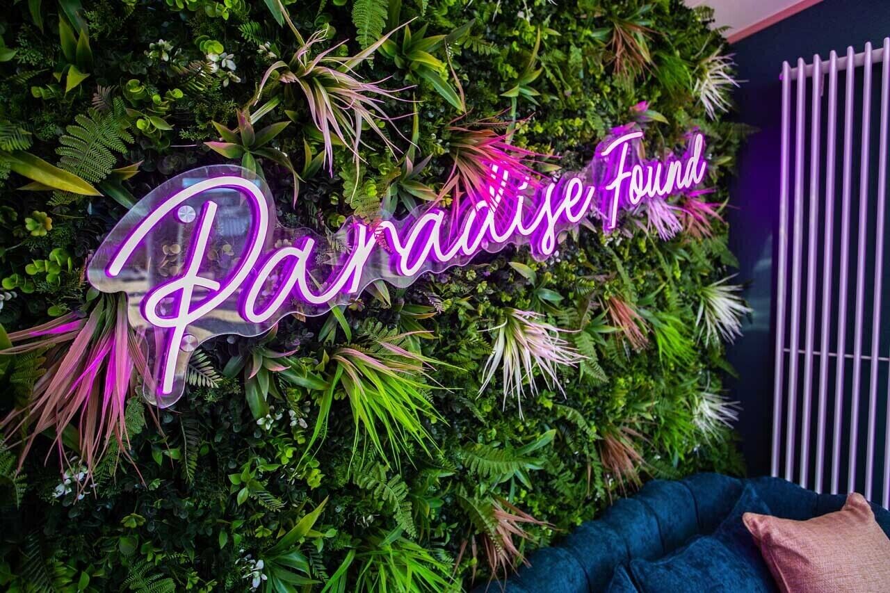 A neon sign with the text 'Paradise Found' against a backdrop of lush green foliage.