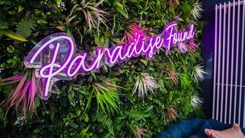 A neon sign with the text 'Paradise Found' against a backdrop of lush green foliage.