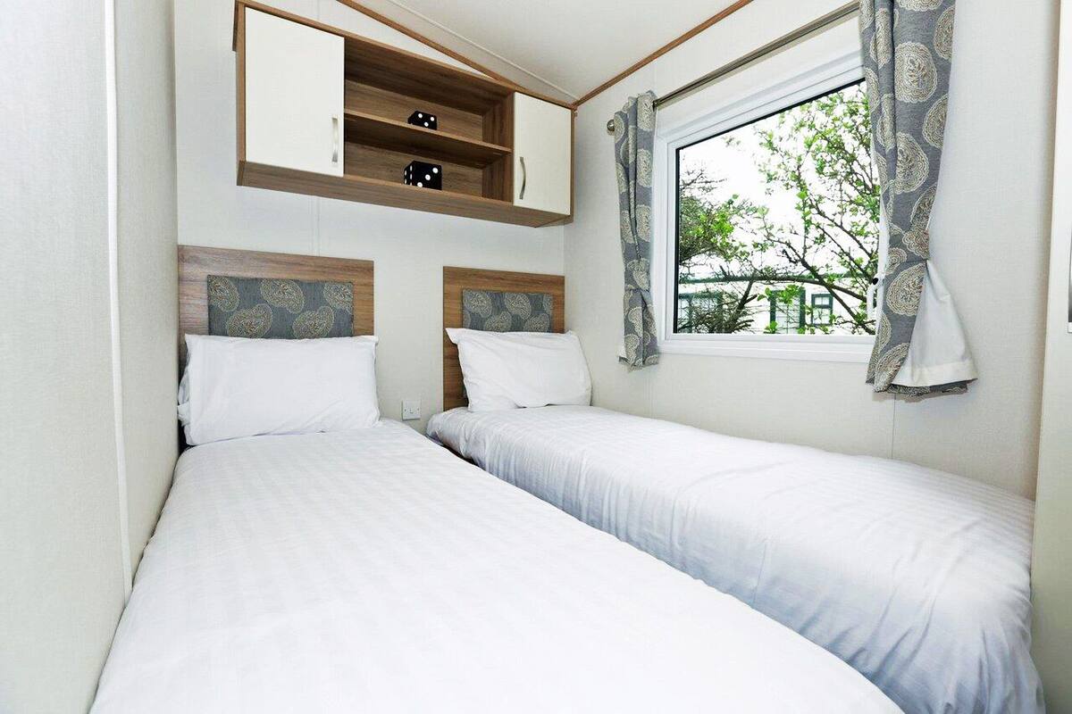Quarto com duas camas de solteiro, uma estante embutida com dados e uma janela com cortinas.