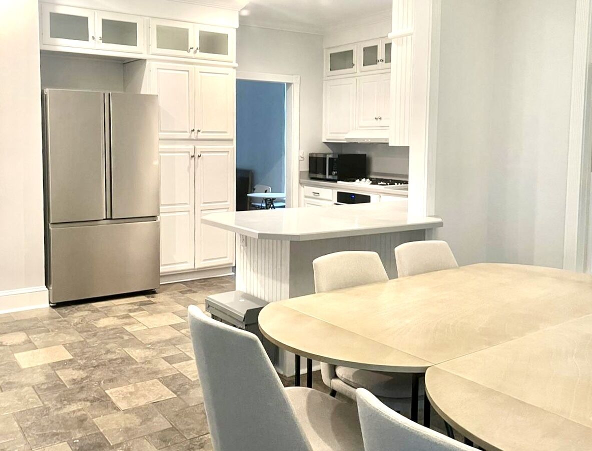 A modern kitchen with white cabinets, a stainless steel refrigerator, a microwave, and a dining area with a round table and chairs.