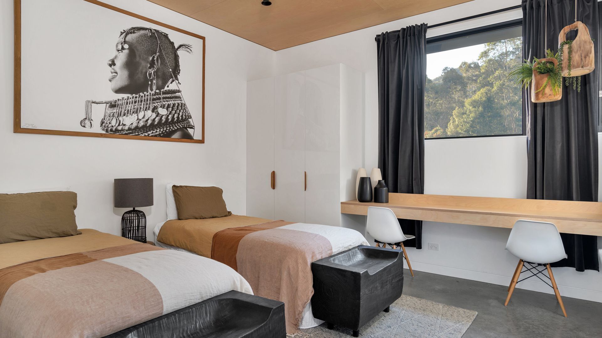 A modern bedroom with two beds, a desk, and a large window with curtains.