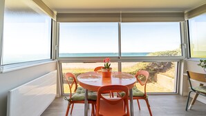 Uma sala de jantar com mesa e cadeiras, vista para a praia e uma janela com persianas.