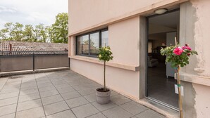 Une terrasse sur le toit avec deux plantes en pot, l’entrée d’un immeuble et une vue sur l’intérieur.