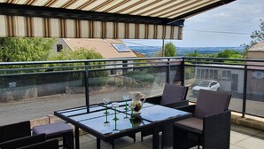 Un balcon avec une table en verre, des chaises en osier et une plante en pot.